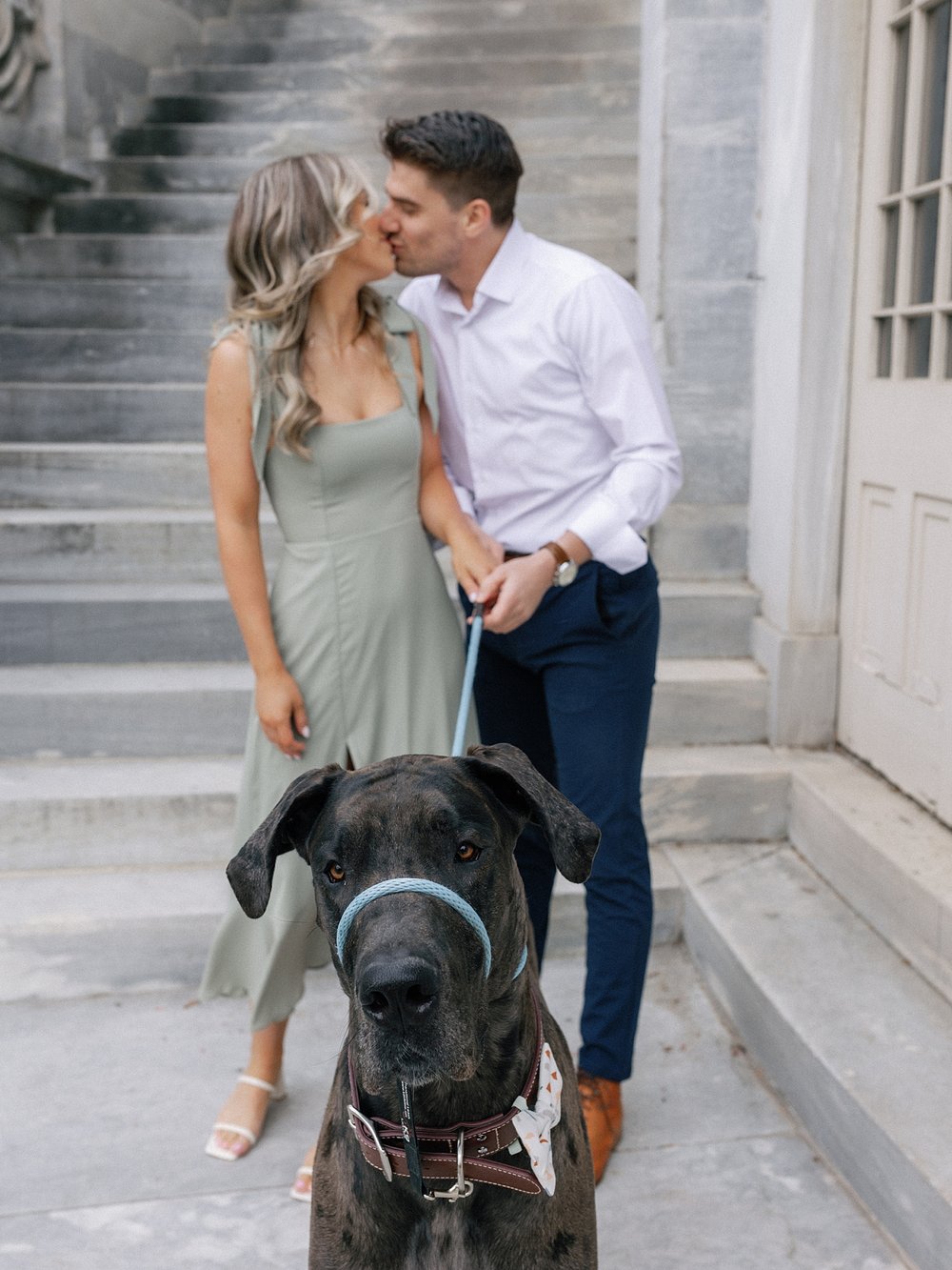 engaged couple kisses in front of steps at the Merchant Exchange Building with Great Dane sitting in front of them