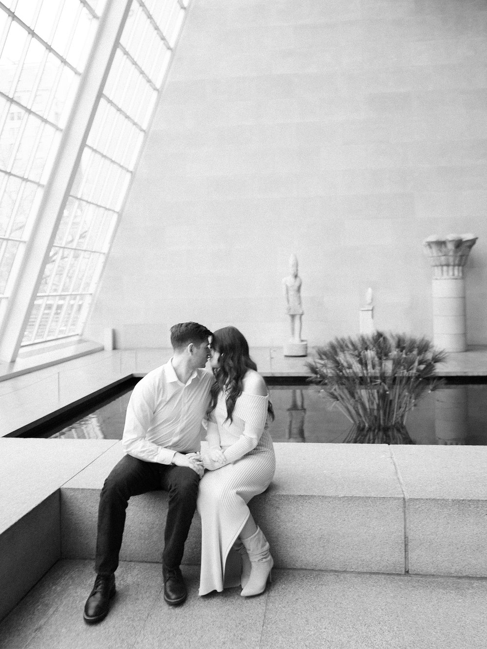 engaged couple sits on bench inside temple of Dendur exhibit in the the Metropolitan Museum of Art