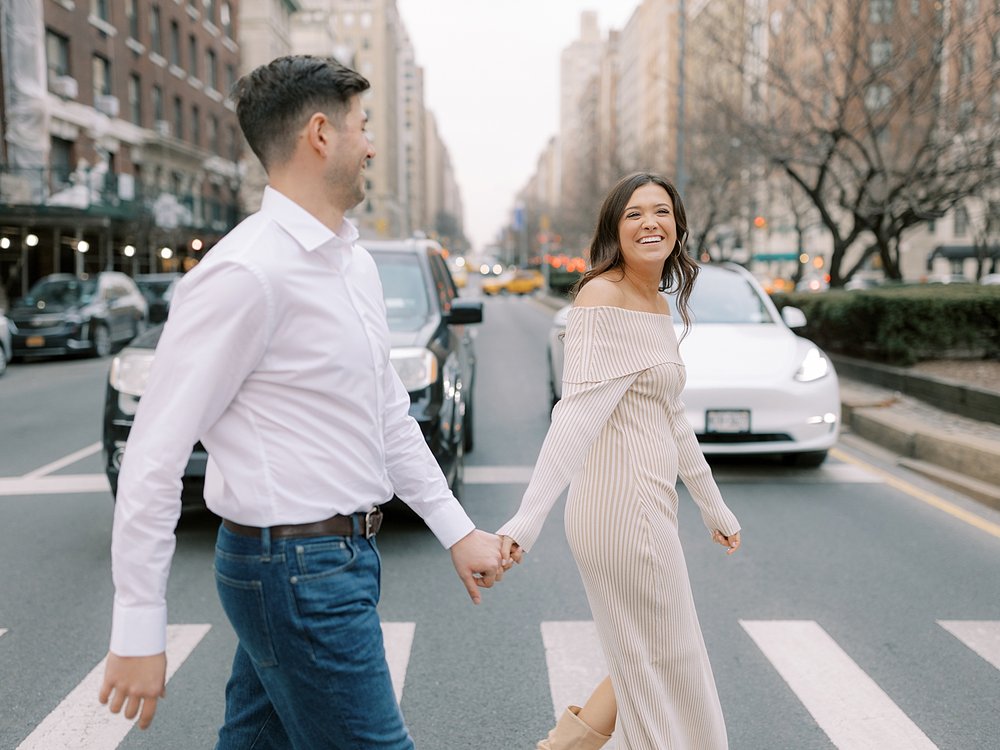 engaged couple holds hands walking across crosswalk on the Upper East Side