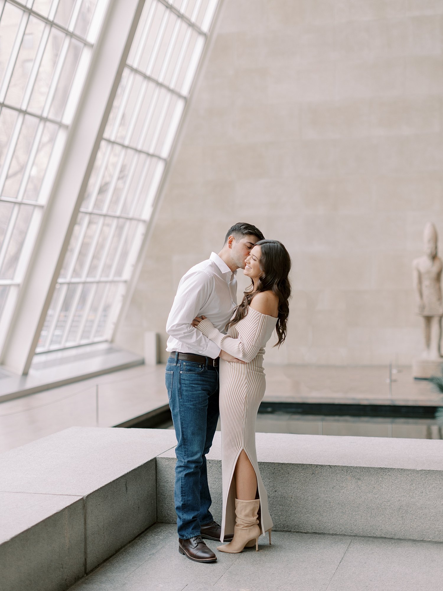 engaged couple kisses near slanted windows inside the the Metropolitan Museum of Art