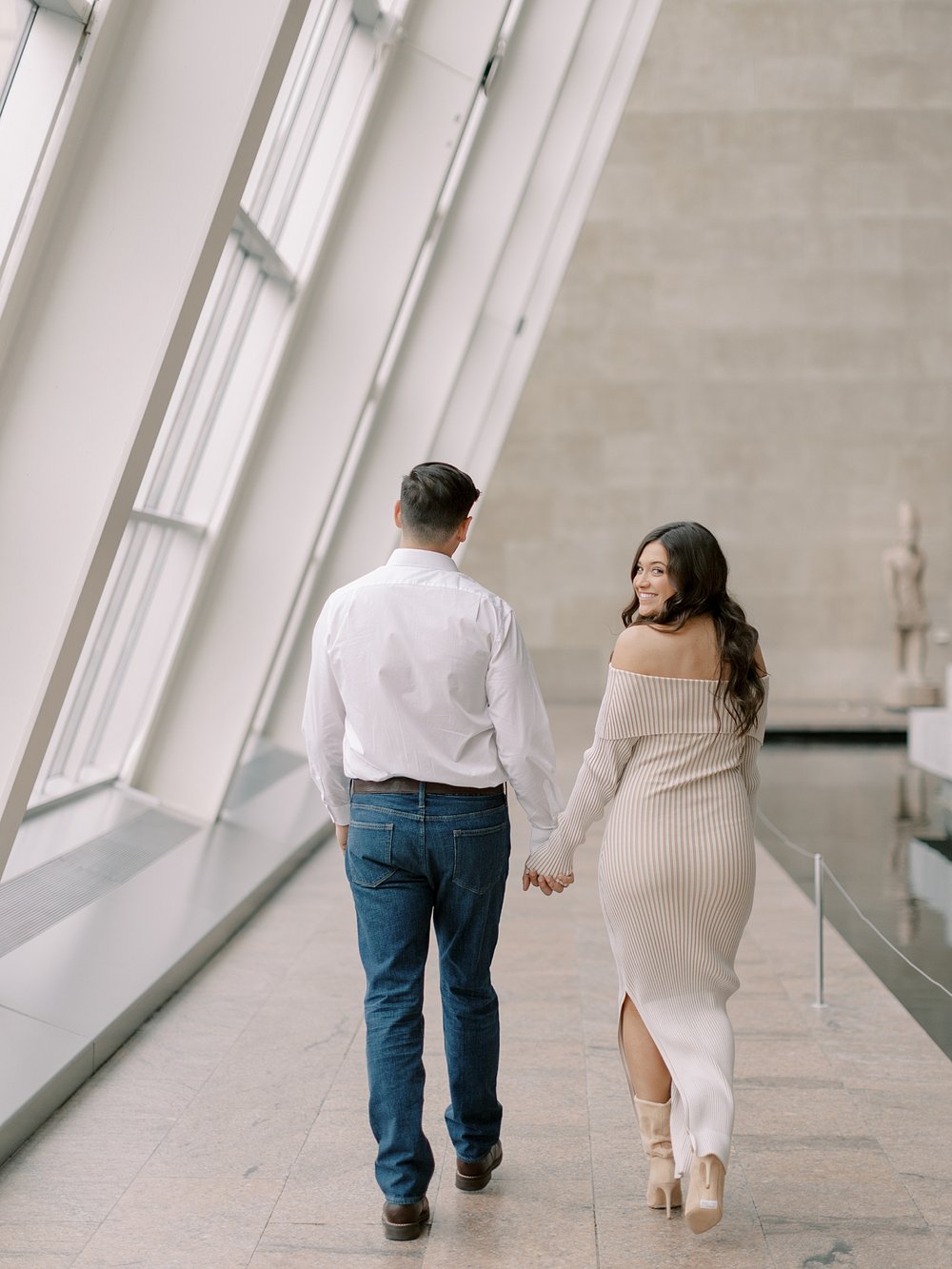 engaged couple holds hands while woman looks over shoulder inside the Metropolitan Museum of Art