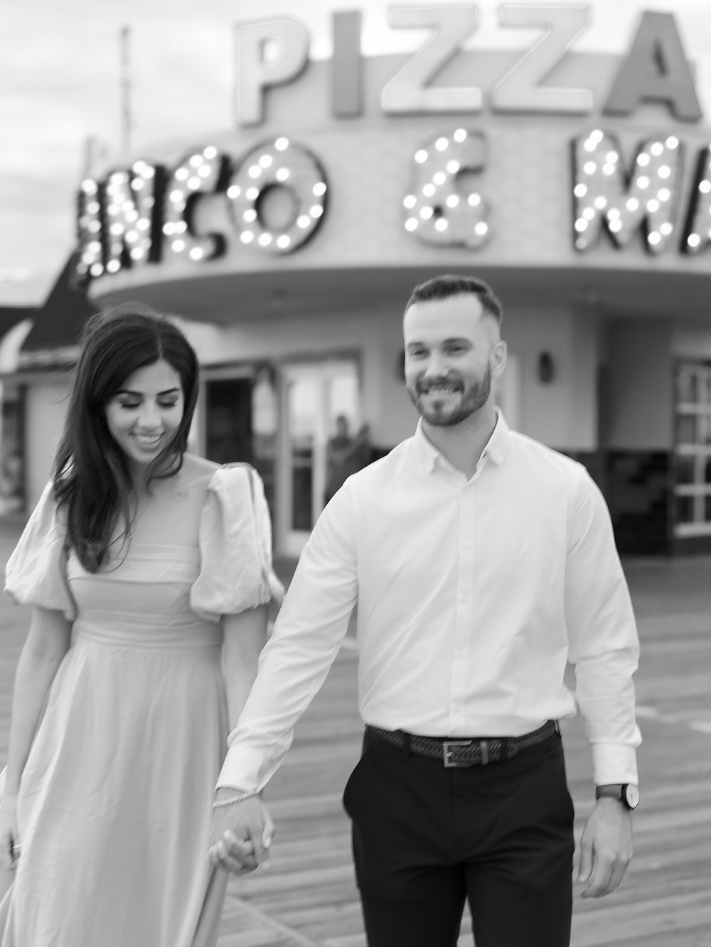 engaged couple walks on Ocean City Boardwalk holding hands during engagement photos 