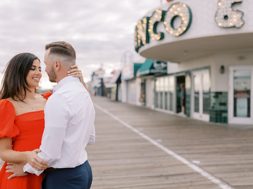 woman in orange dress hugs man to her with her hand around his neck on Ocean City Boardwalk