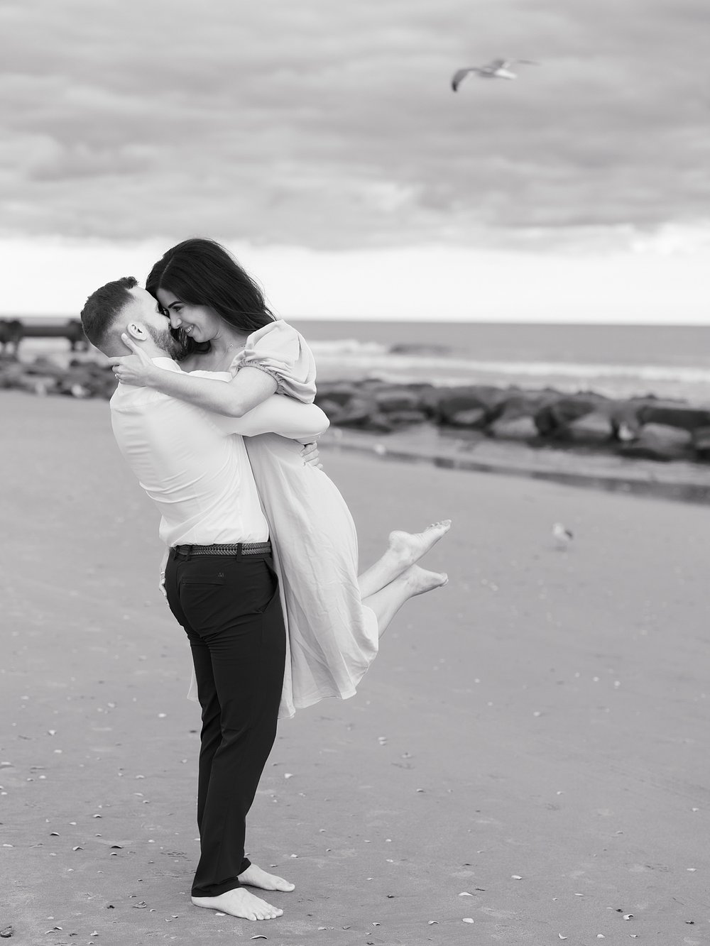 man lifts up fiancee on beach during Ocean City Boardwalk engagement portraits 