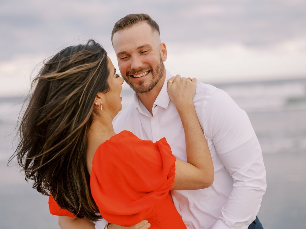 engaged couple laughs while wind blows bride's hair around on beach in Ocean City NJ
