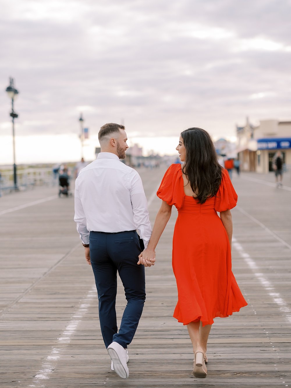 engaged couple holds hands walking down boardwalk at sunset in Ocean City NJ