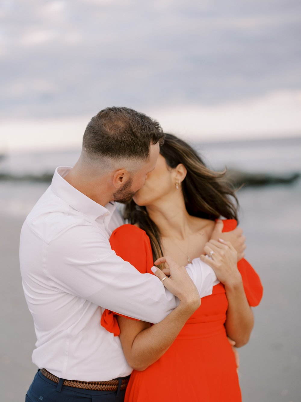 engaged couple kisses while wind lifts woman's hair on beach in Ocean City NJ