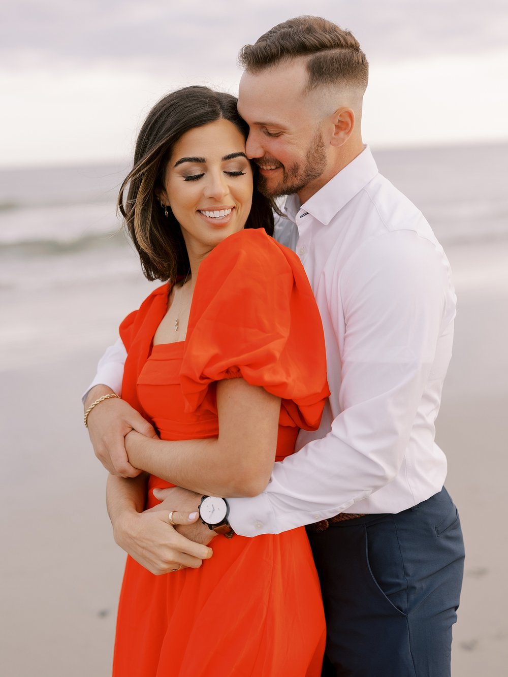 man hugs woman from behind snuggling during beach engagement portraits in Ocean City NJ