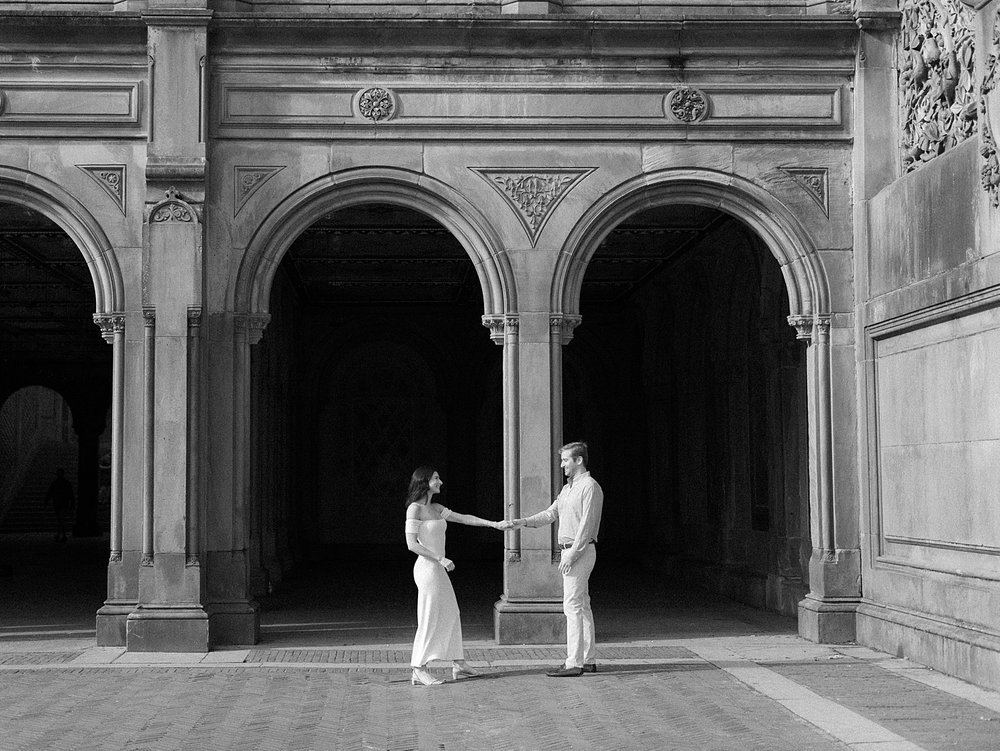 black and white photo of couple holding hands in front of arches in Central Park