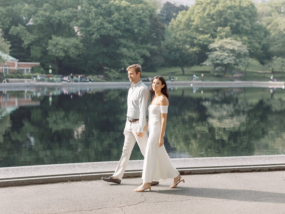 engaged couple holds hands walking by lake in Central Park