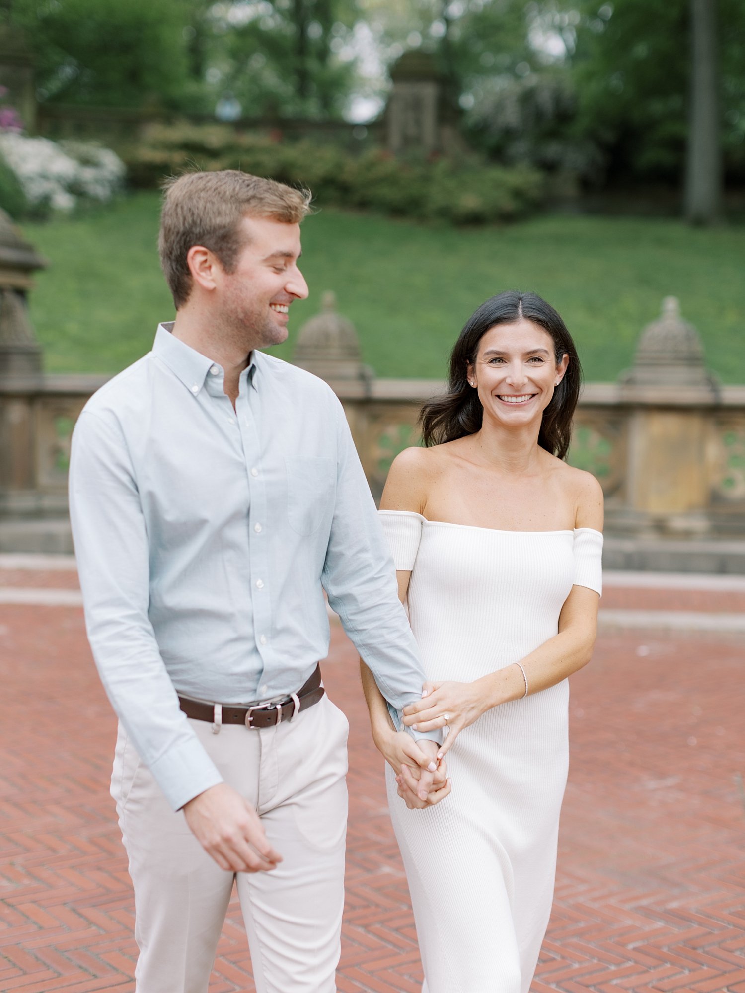 man smiles at fiancee holding her hand near steps inside Central Park