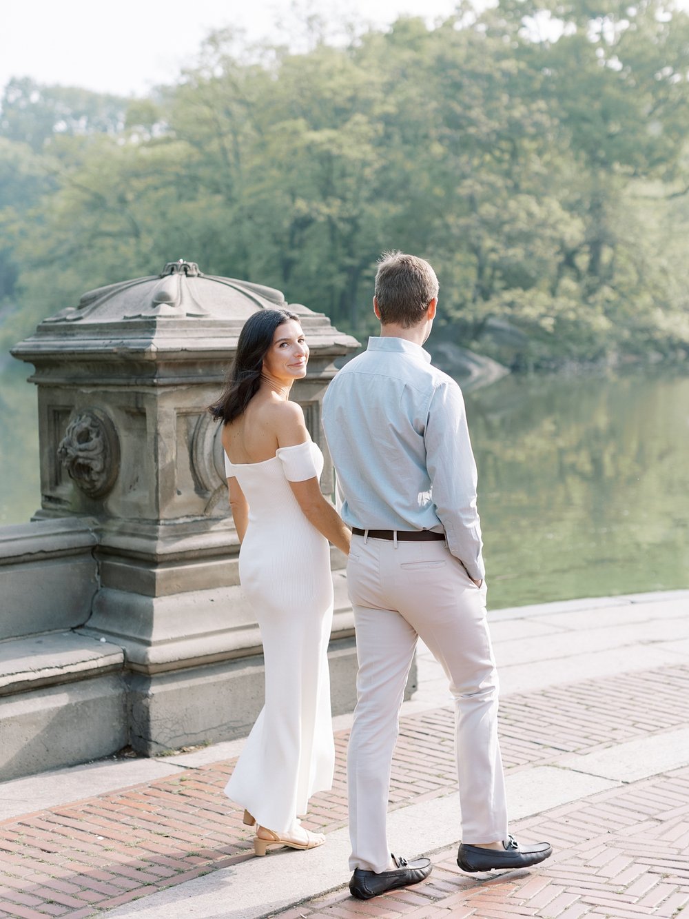 engaged couple holds hands walking along lake inside Central Park