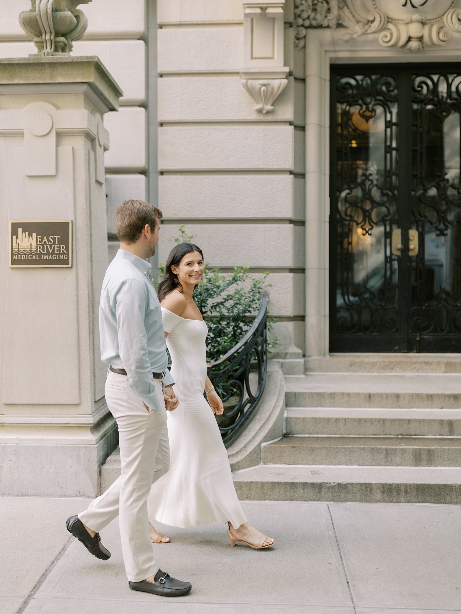 engaged couple holds hands walking by houses on the Upper East Side in New York City