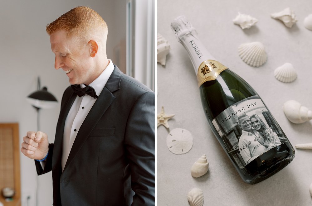 groom stands in black suit jacket next to champagne bottle with custom label of couple 