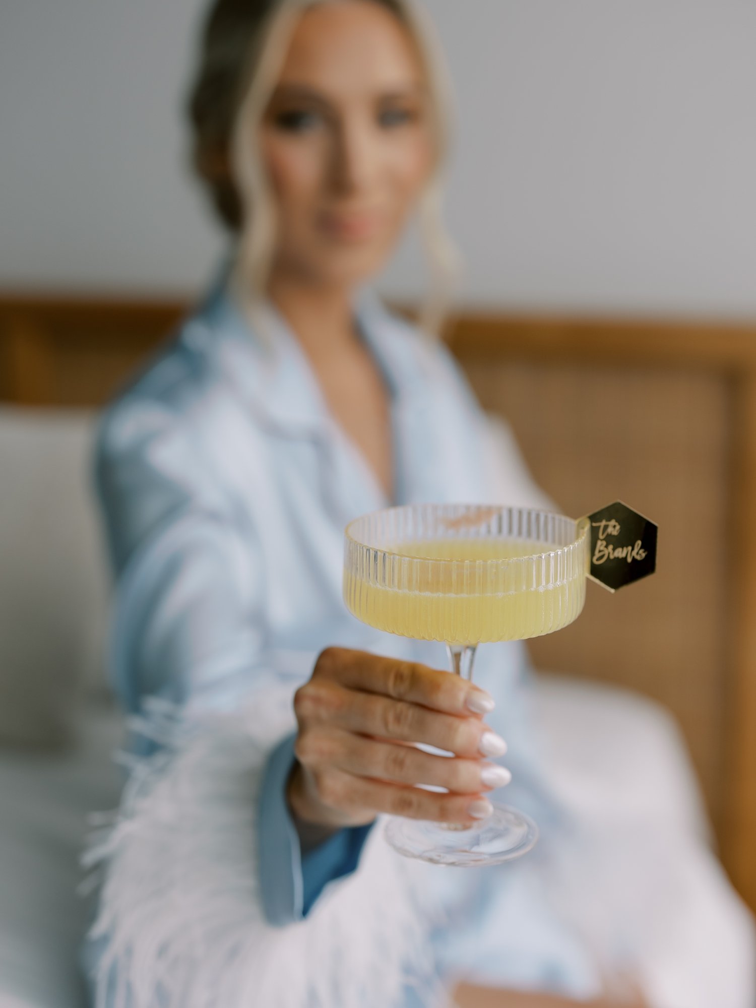 bride holds out mimosa with custom card on edge of glass
