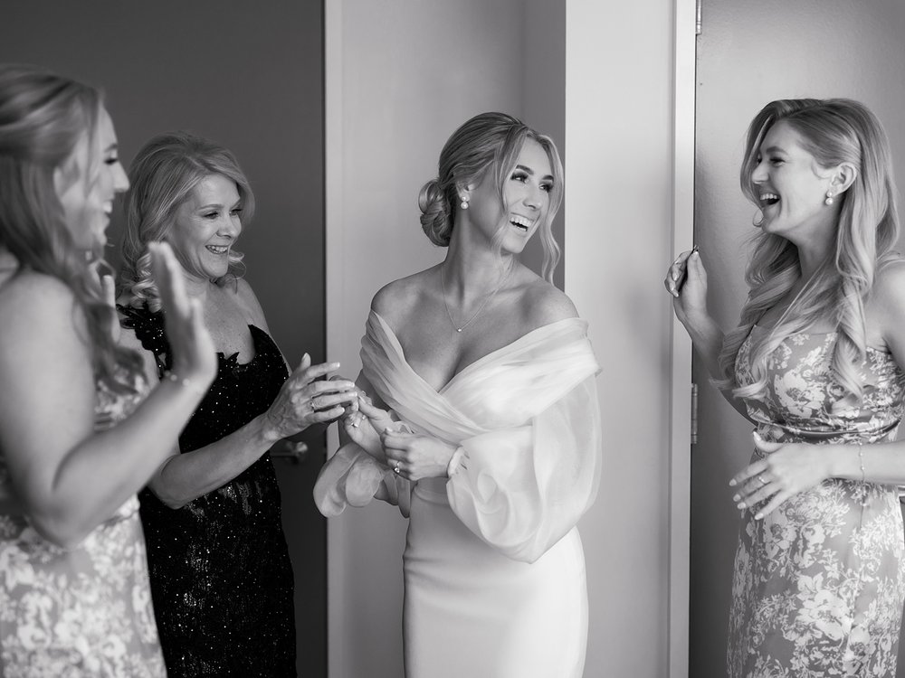 bride smiles at bridesmaids showing off back of wedding gown