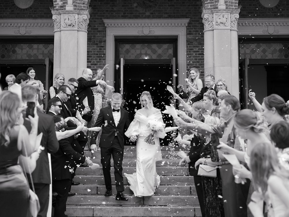 bride and groom walk down steps while guests cheer and throw petals