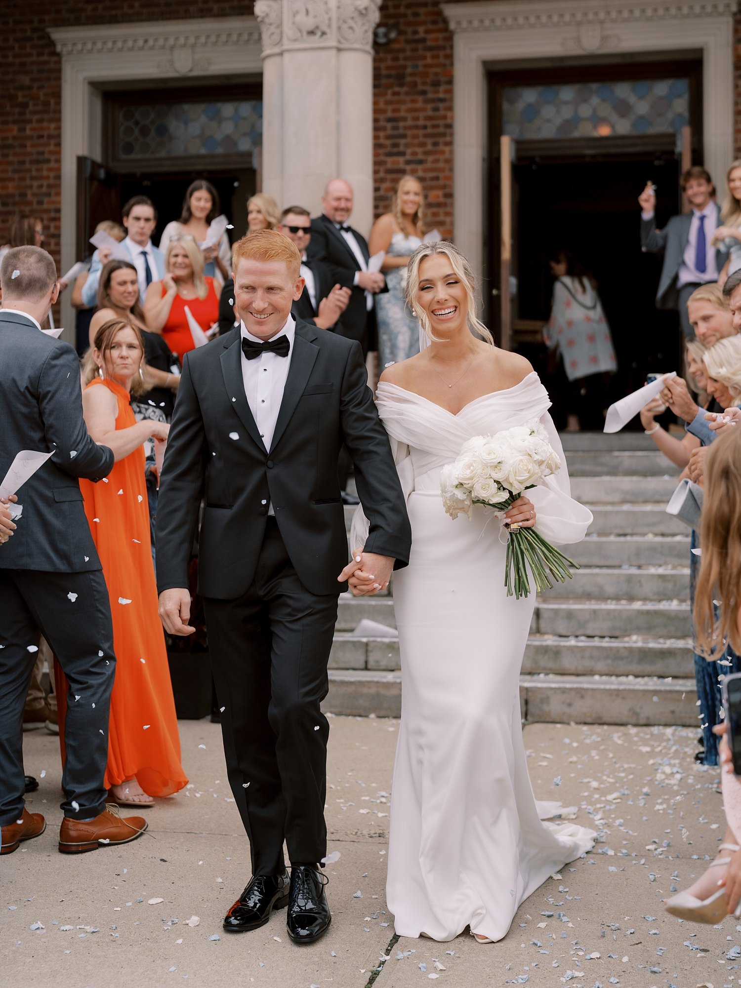 bride and groom hold hands walking through guests on steps outside Long Island NY church