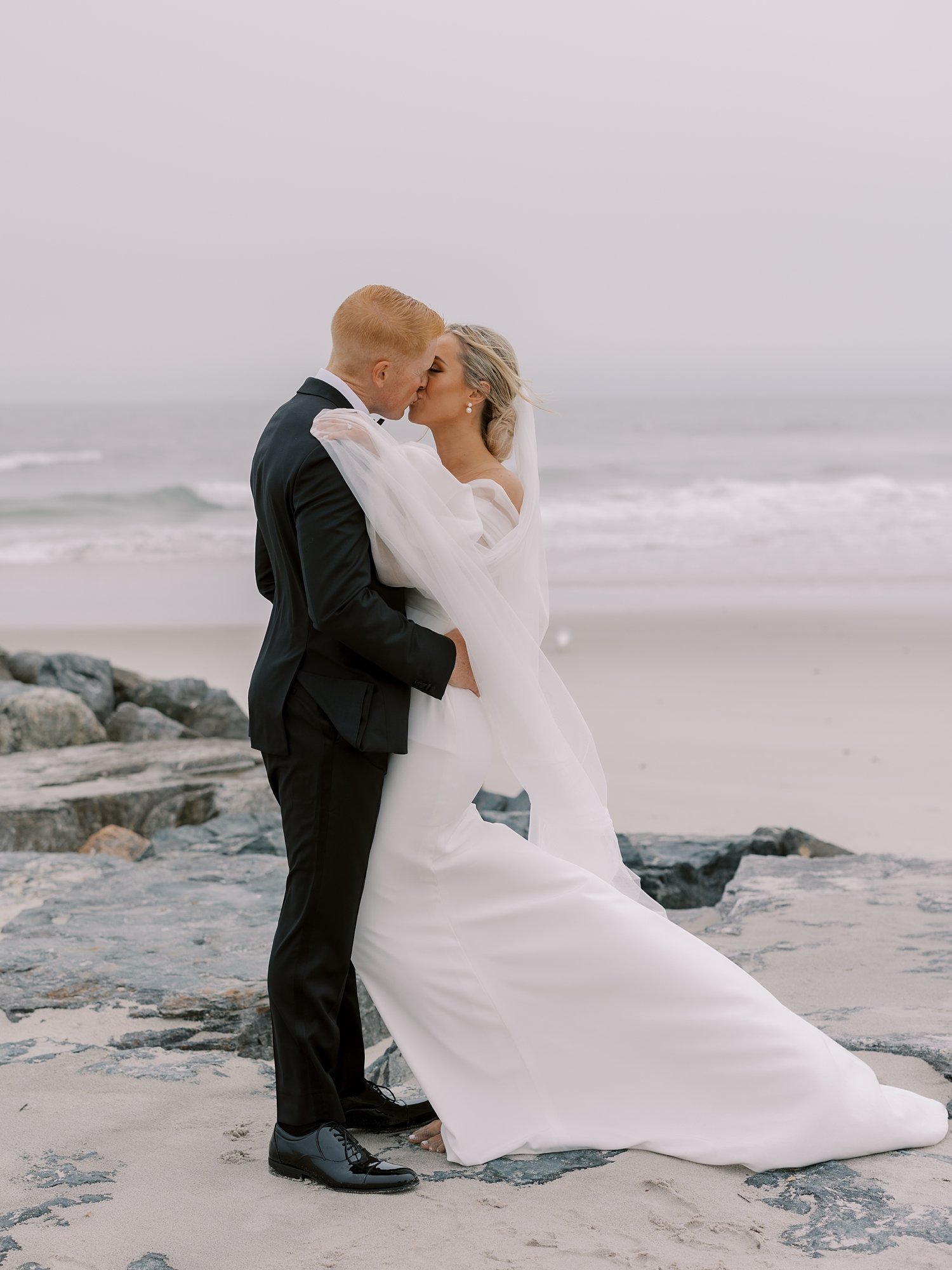 newlyweds kiss along rocks on edge of Long Island beach