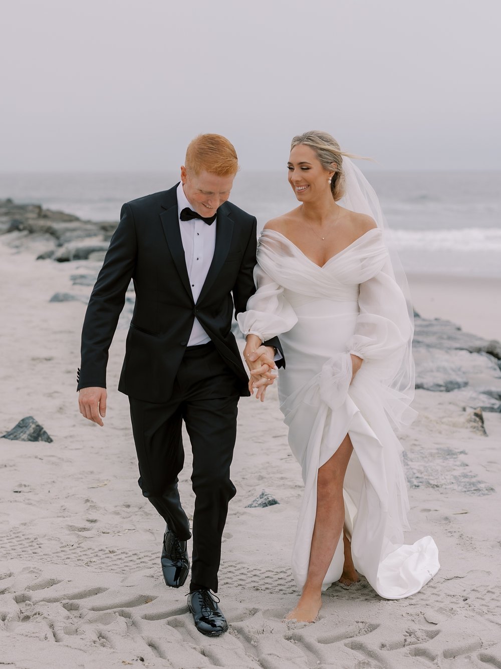 bride and groom hold hands walking and laughing on Long Island beach