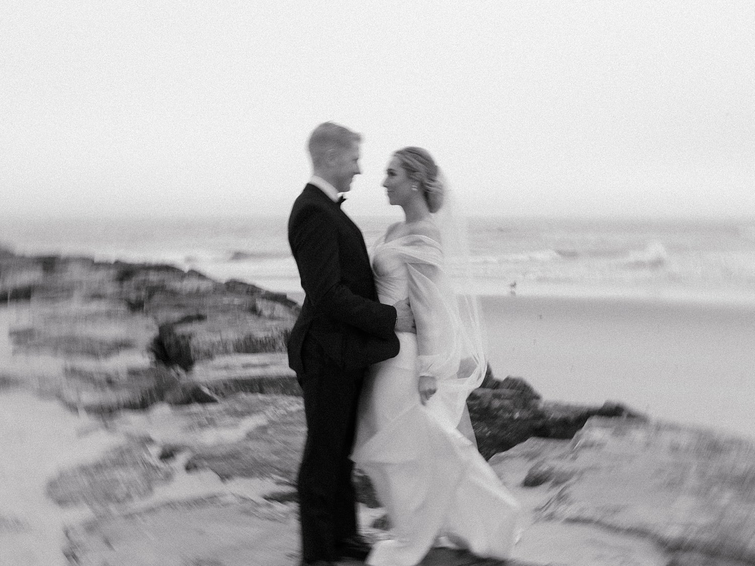 bride and groom smile together in front of rocks on Long Island beach