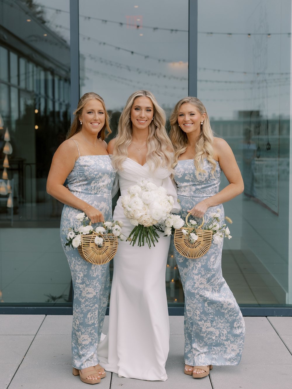 bride smiles with two bridesmaids in blue and white gowns outside the Rockaway Hotel