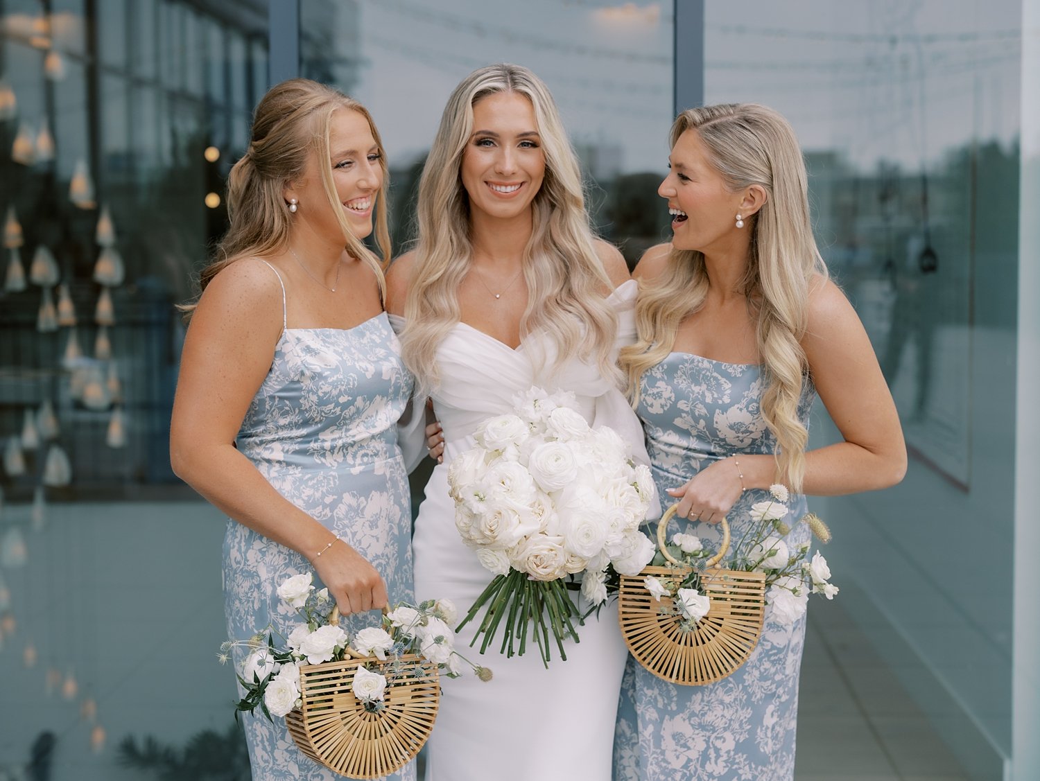 bride smiles with bridesmaids in blue and white gowns carrying baskets outside the Rockaway Hotel