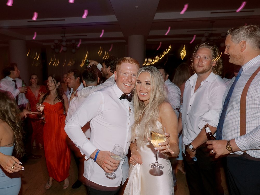 bride and groom hug on dance floor with glass of wine during Long Island beach wedding reception