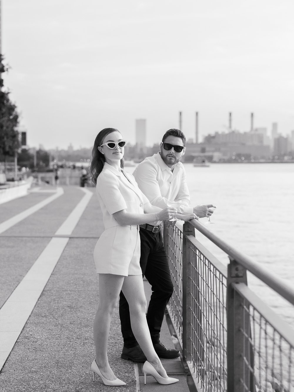 engaged couple leans against fence in Greenpoint Waterfront Park