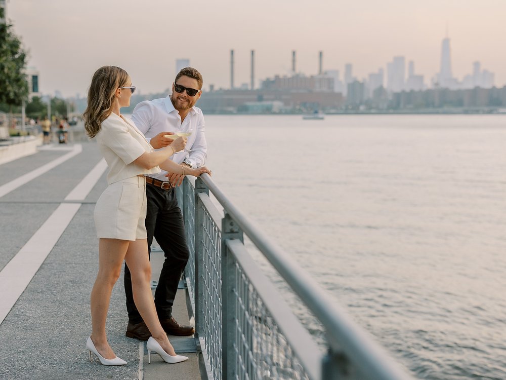 engaged couple look at each other holding champagne at Greenpoint Waterfront Park