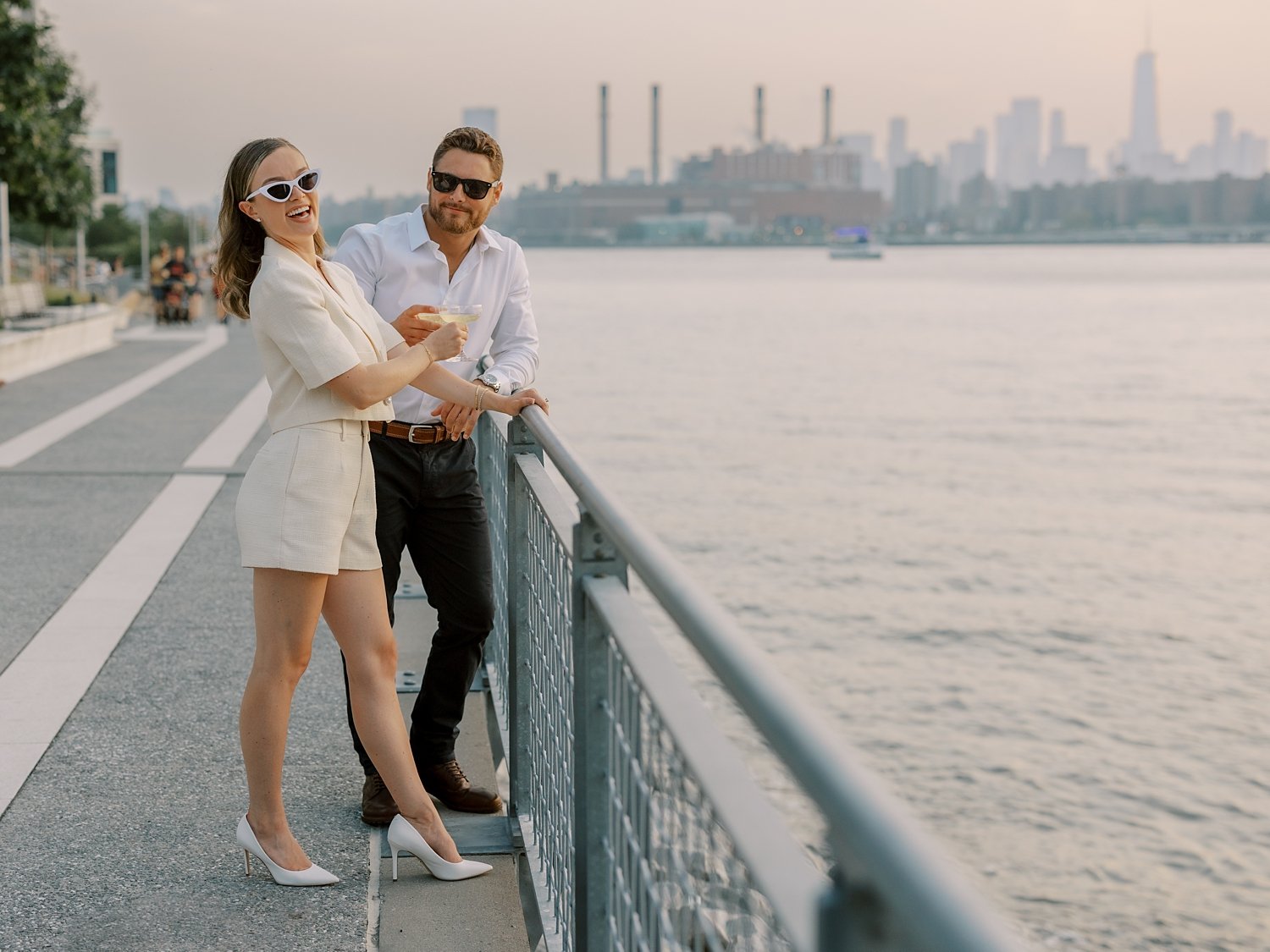 man leans against fence at Greenpoint Waterfront Park with bride next to him