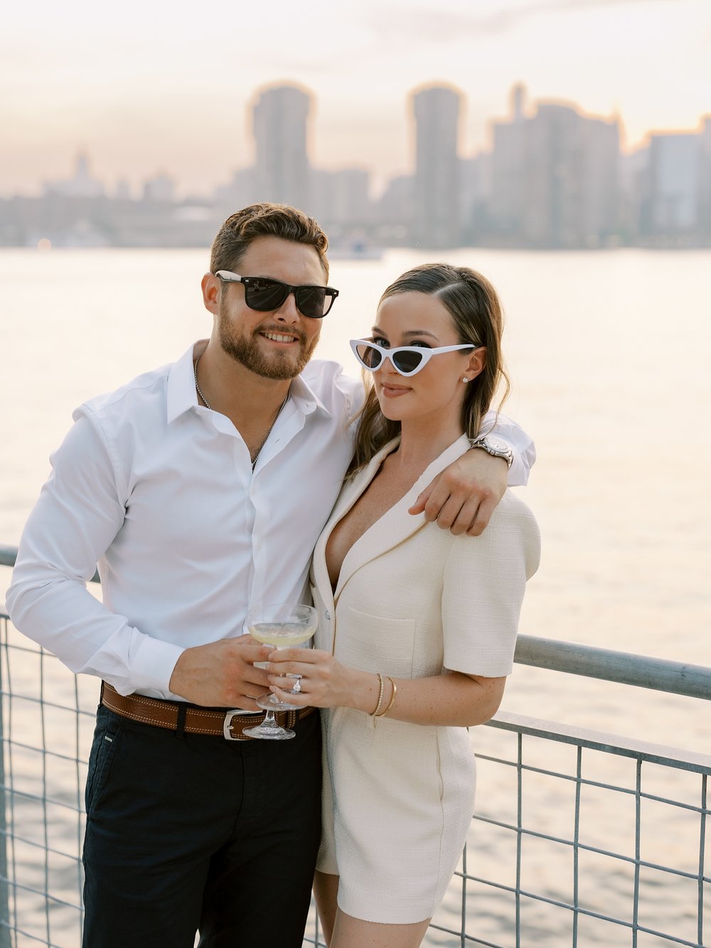 man hugs woman around shoulders wearing white sunglasses