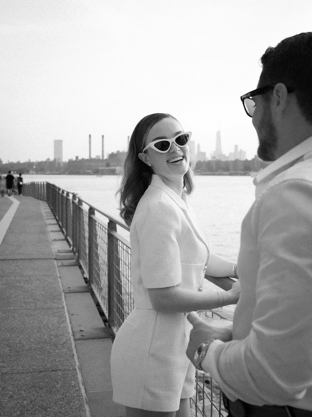 woman in white retro sunglasses looks over shoulder holding on to fence in Greenpoint Waterfront Park