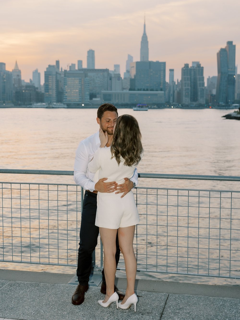 woman hugs man in front of Manhattan skyline in Greenpoint Waterfront Park