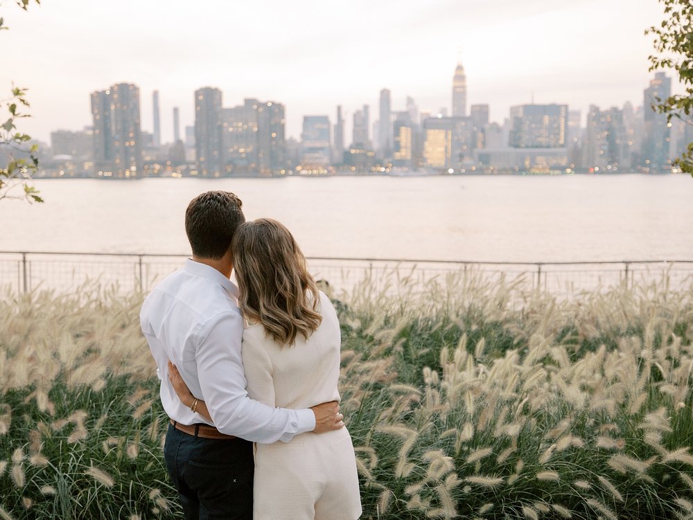 engaged couple hugs looking at NYC skyline in Manhattan 