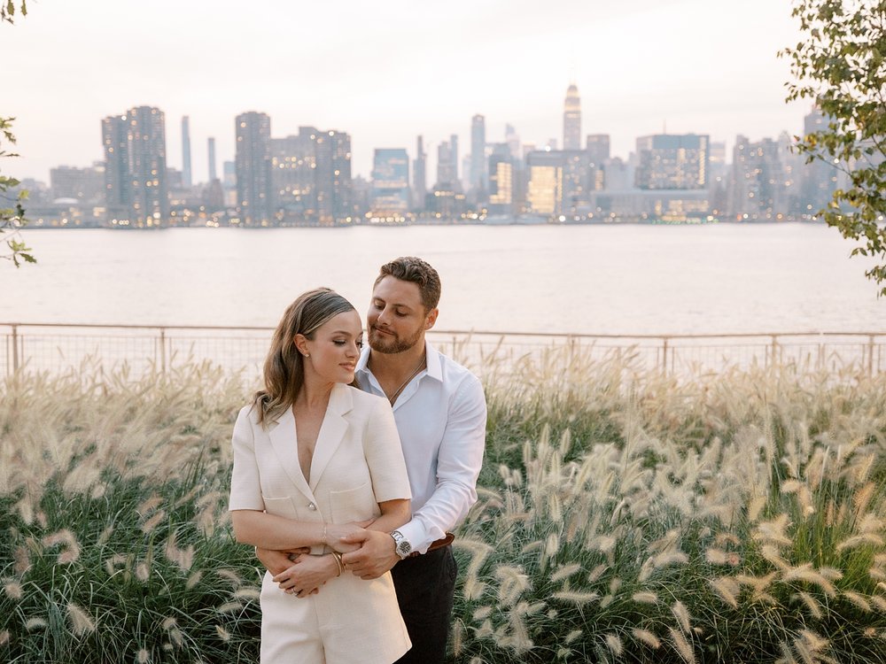man hugs woman from behind in NYC engagement session at Greenpoint Waterfront Park