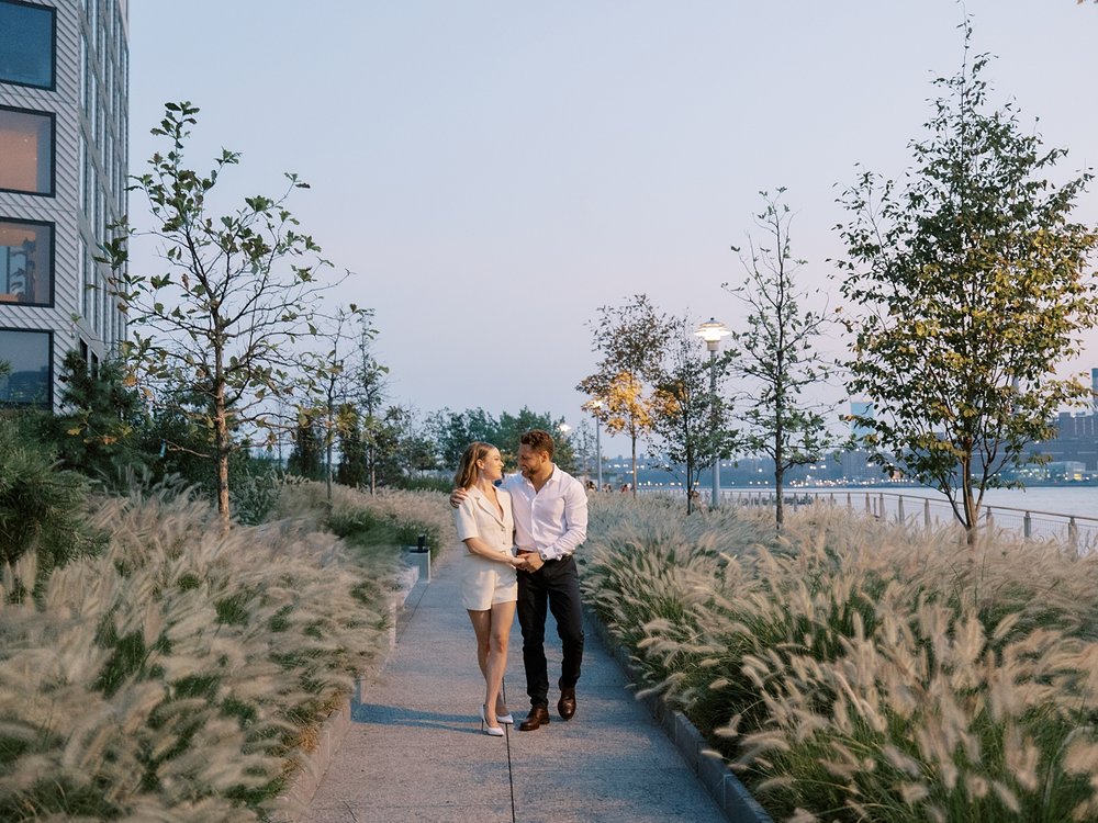 engaged couple walks down sidewalk in Greenpoint Waterfront Park