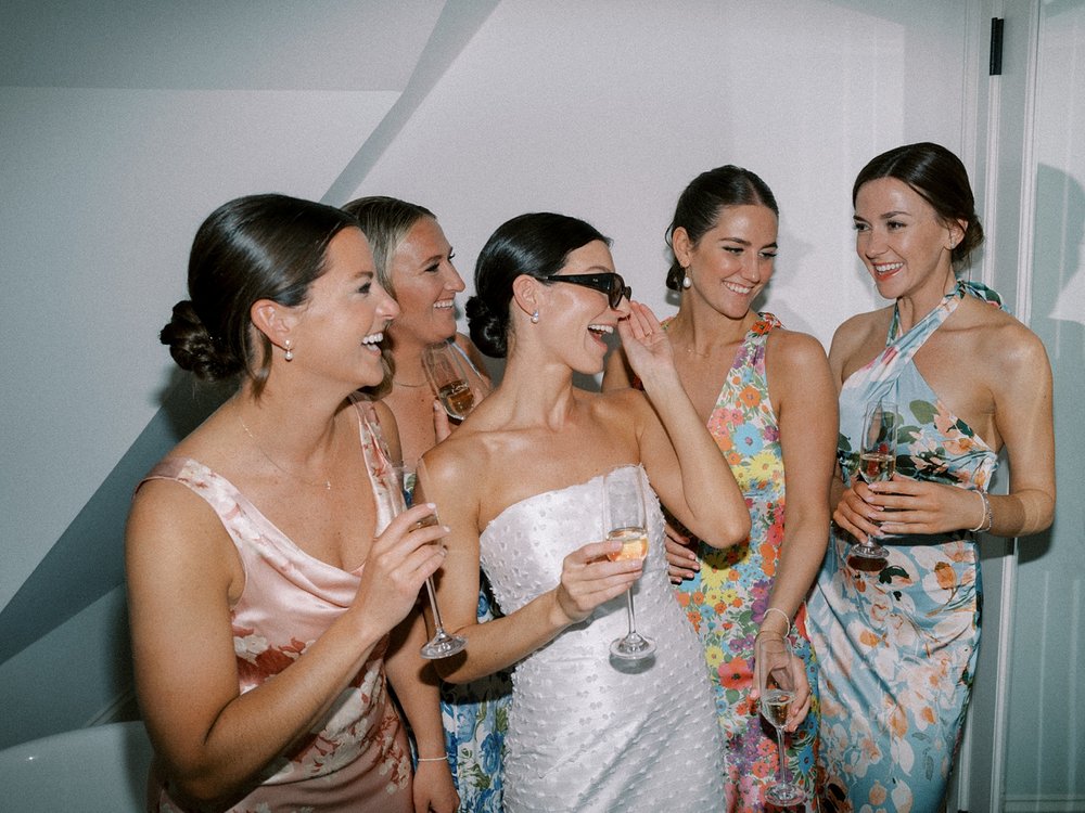 bride in sunglasses laughs with mismatched flower gowns