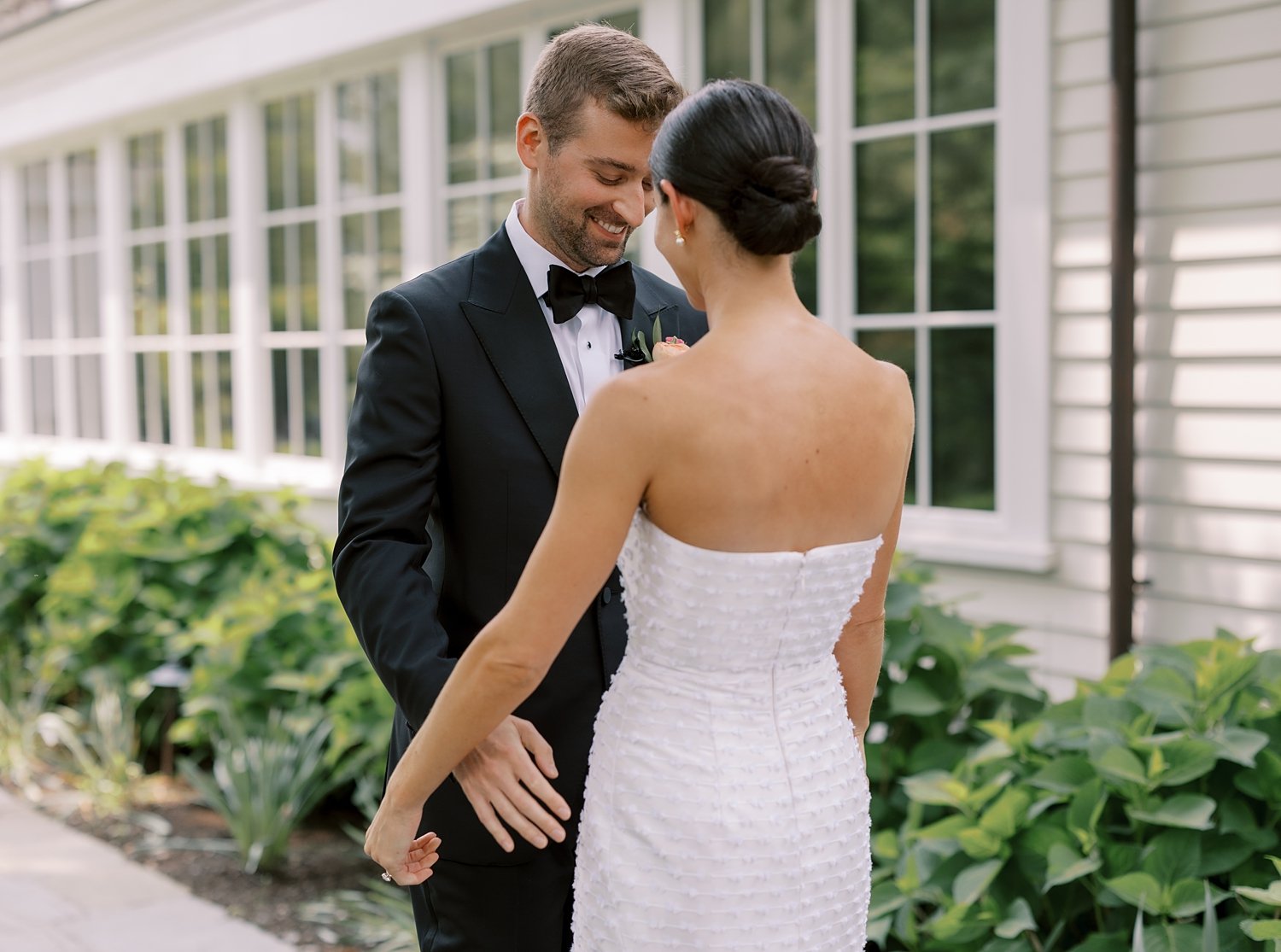 groom looks down at bride's wedding dress at The Country Club of New Canaan