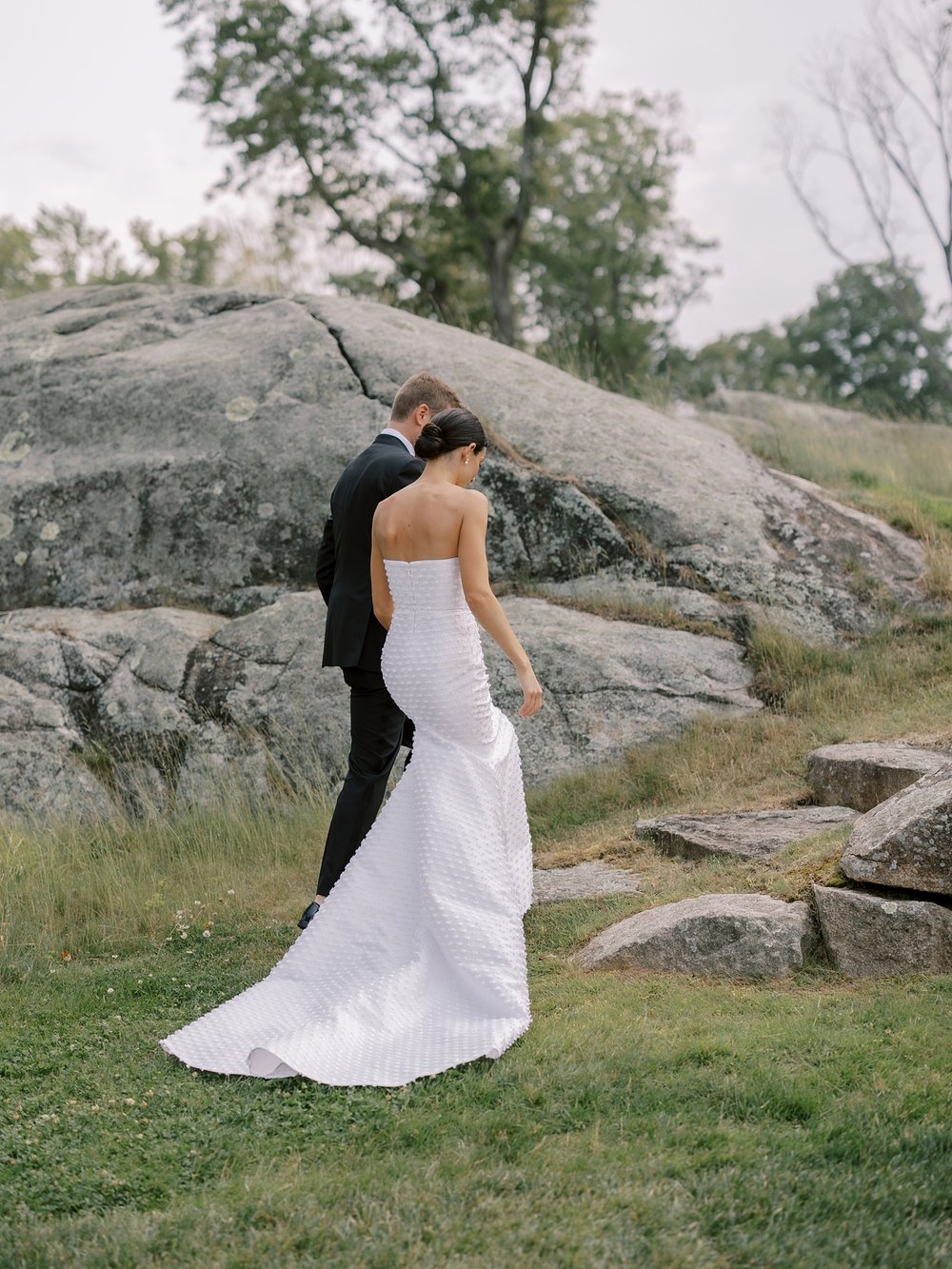 bride and groom hold hands walking up rocks and lawn at The Country Club of New Canaan