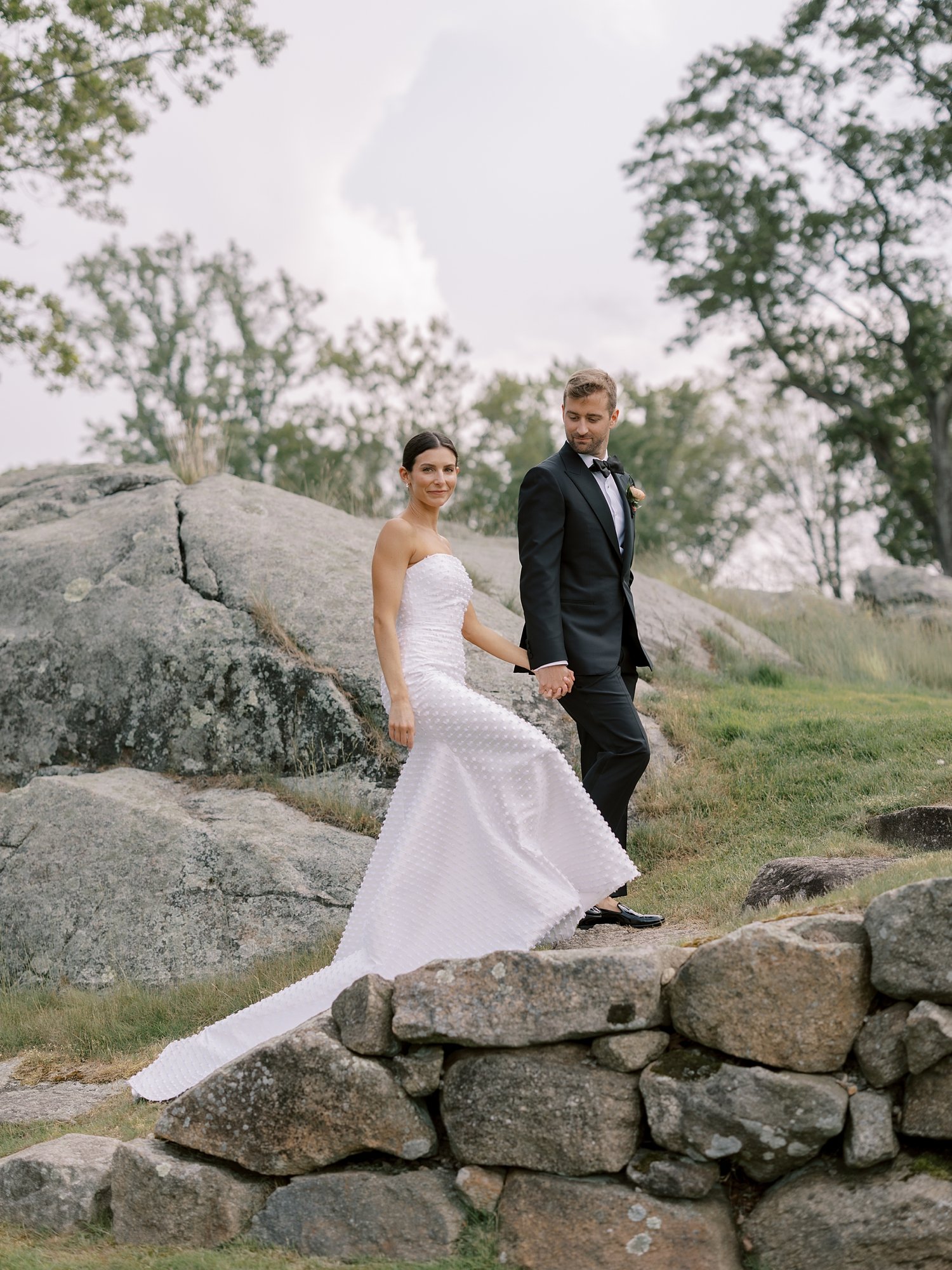 groom leads bride up rock steps outside The Country Club of New Canaan