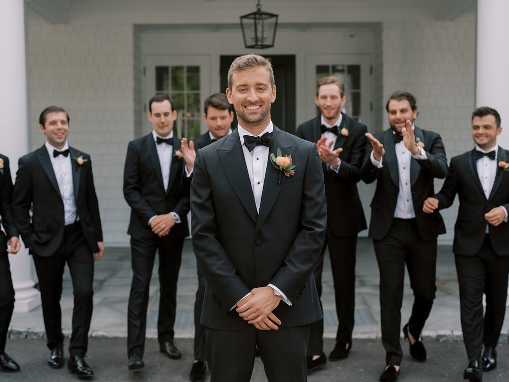 groom in suit poses in front of groomsmen outside The Country Club of New Canaan