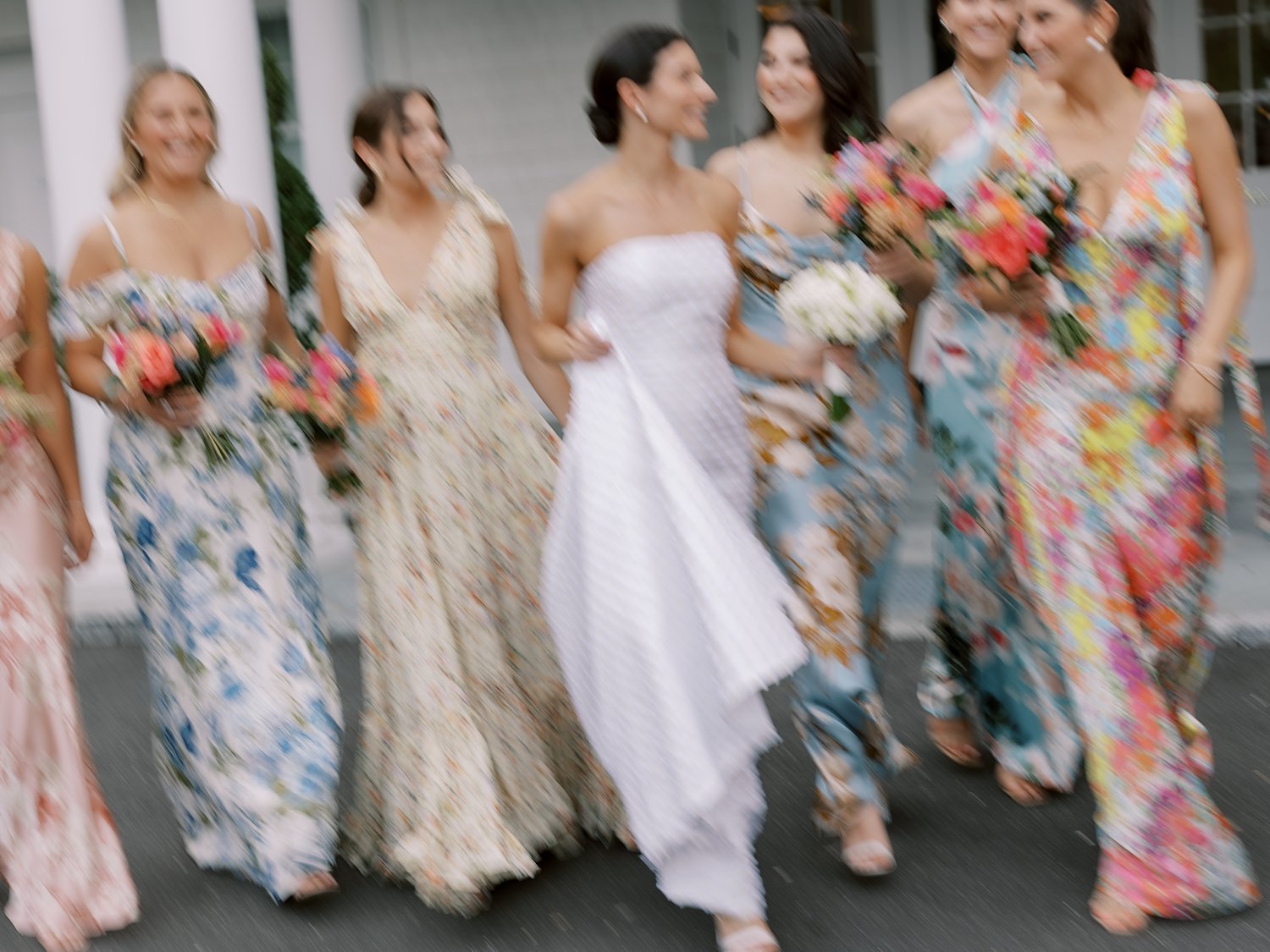 blurry photo of bride walking with bridesmaids in mismatched floral gowns