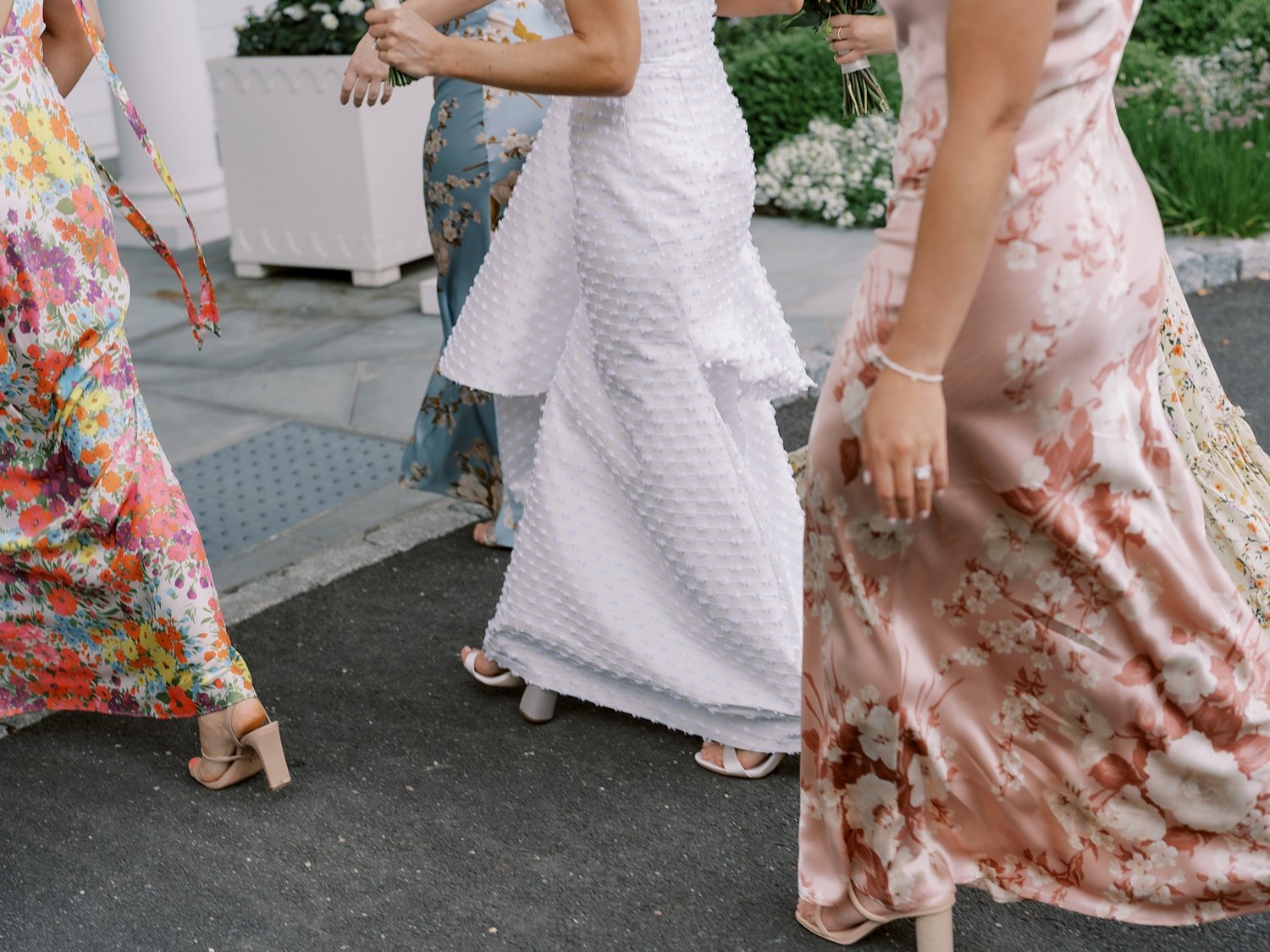 bride walks with bridesmaids in pink and white flower gowns outside The Country Club of New Canaan