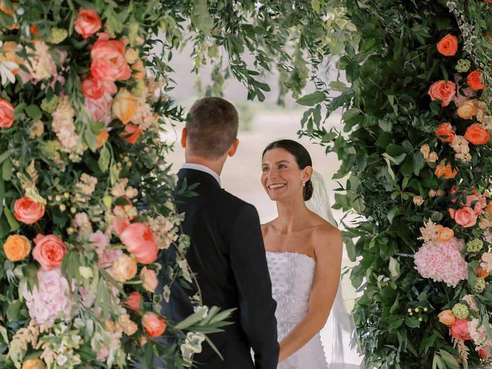newlyweds hold hands by flower arbor for ceremony at The Country Club of New Canaan