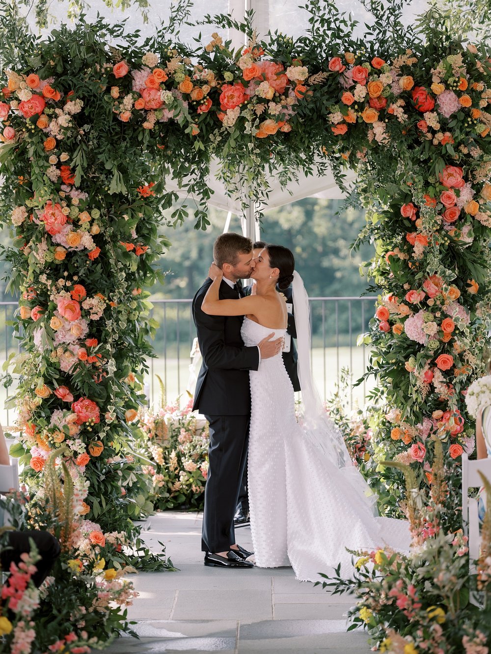bride and groom kiss under floral arbor covered in pink and orange flowers 