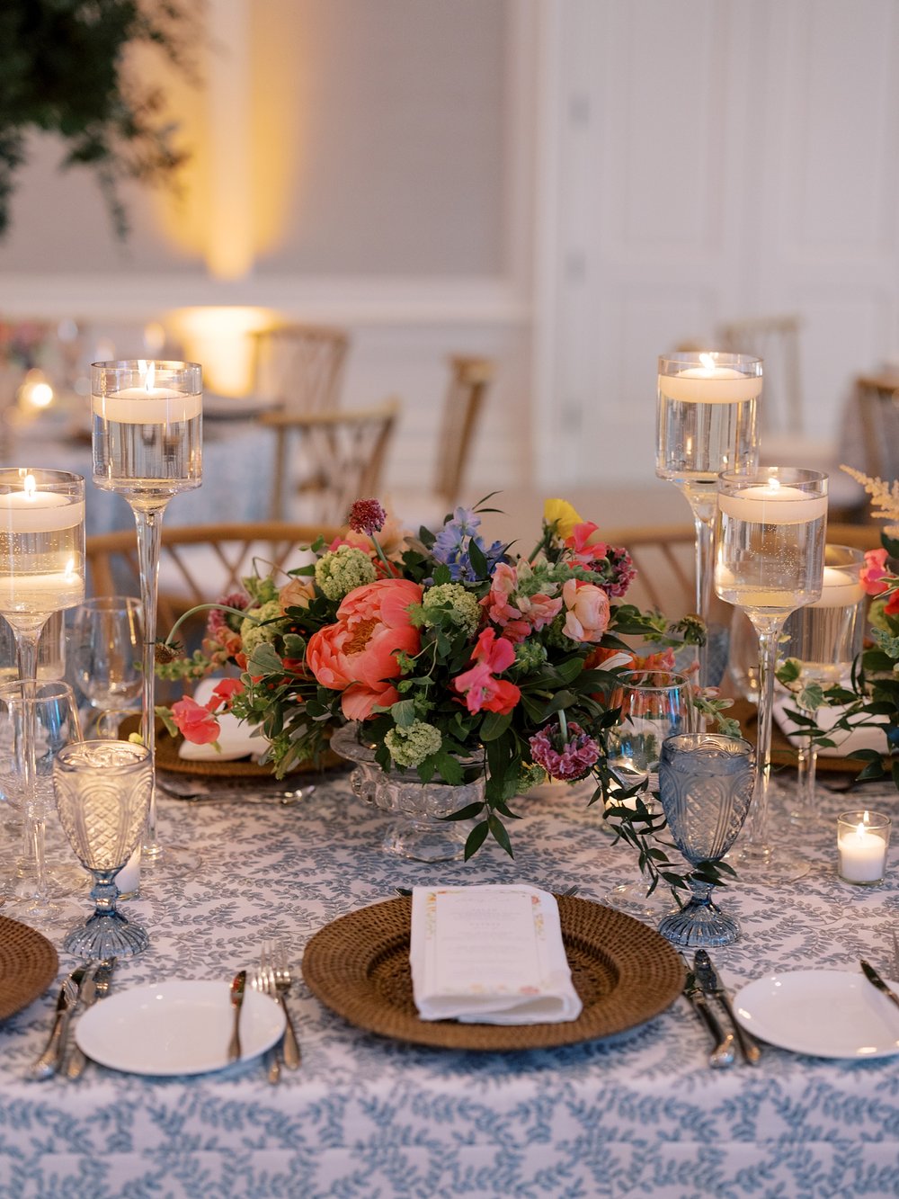 place setting with white napkin on gold charger in front of bright flowers 