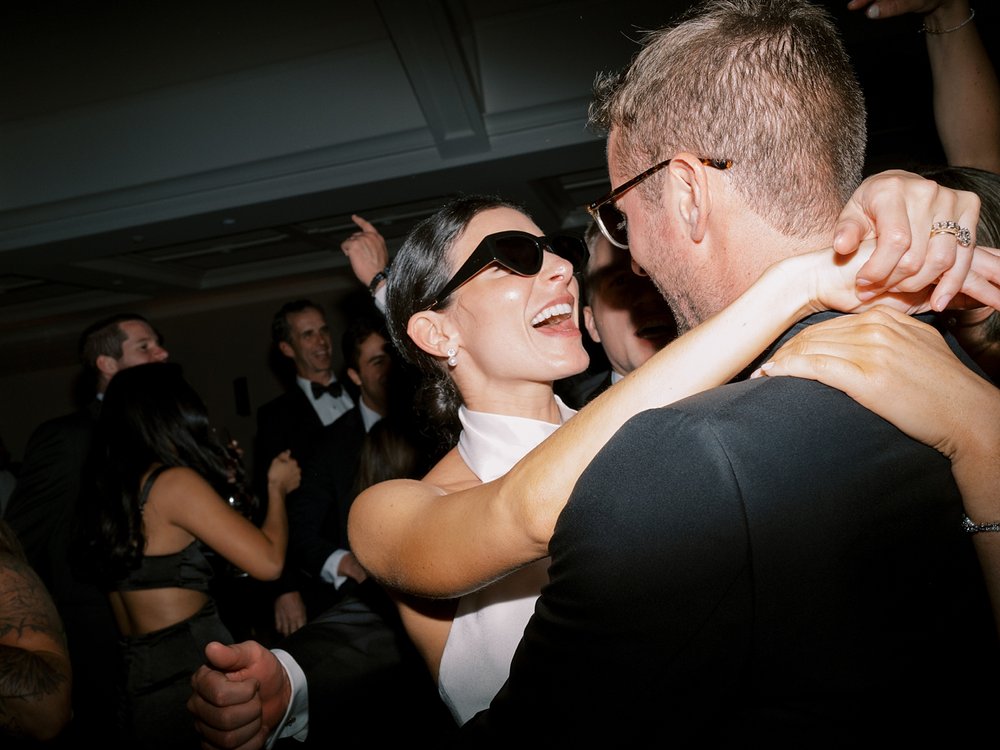 bride in sunglasses looks up at groom smiling during New Canaan wedding reception