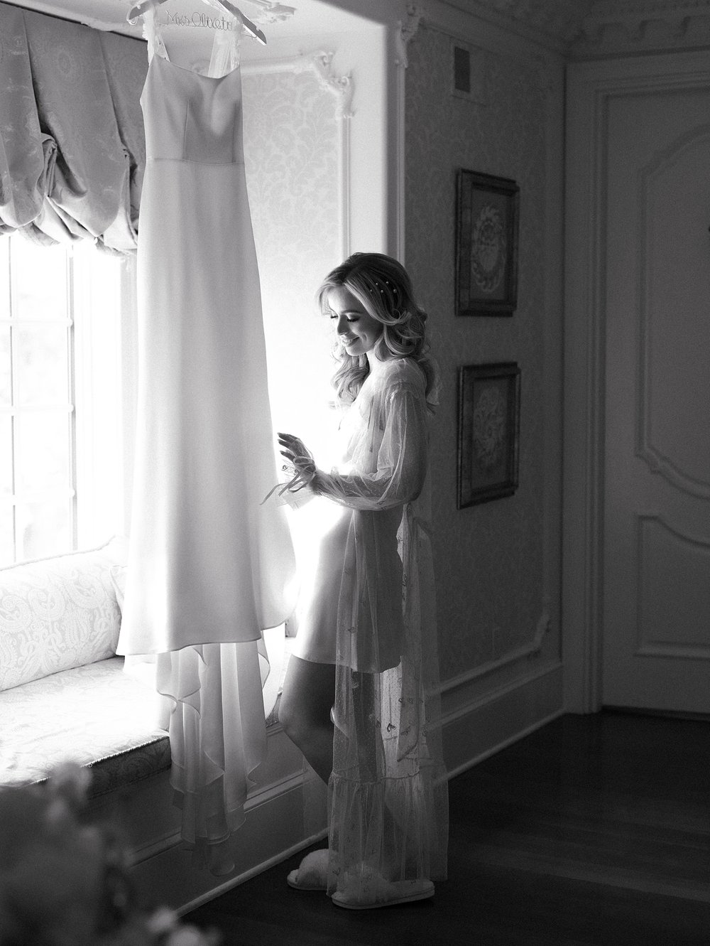 bride looks at wedding dress hanging in window at the Ashford Estate