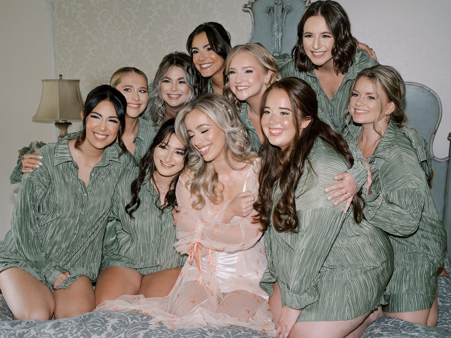 bride poses with bridesmaids in sage green robes on bed at the Ashford Estate